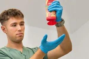 Bauer drückt Duschgel aus einer Flasche auf seine Hand, die von einem Handschuh geschützt wird.