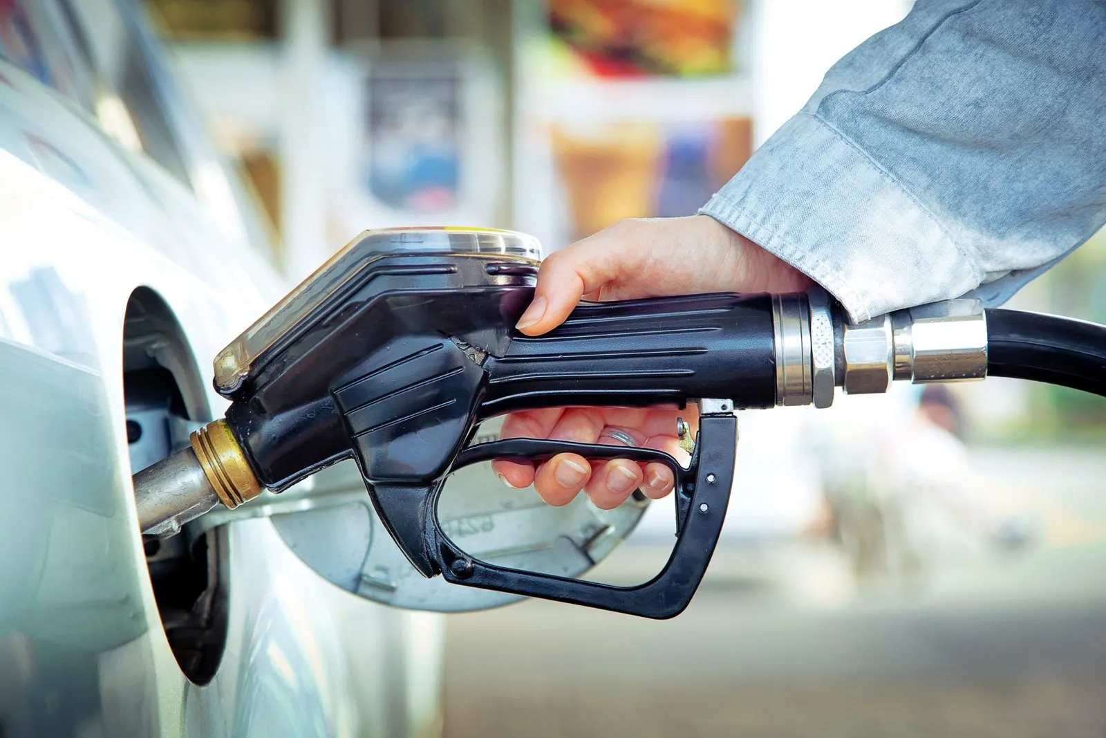 Eine Frau tankt ihr Auto an der Tankstelle und hält dabei den Zapfhahn in der Hand.