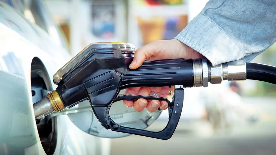 Eine Frau tankt ihr Auto an der Tankstelle und hält dabei den Zapfhahn in der Hand.