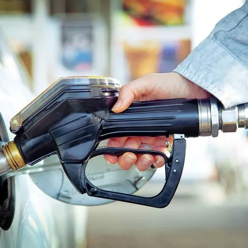Eine Frau tankt ihr Auto an der Tankstelle und hält dabei den Zapfhahn in der Hand.