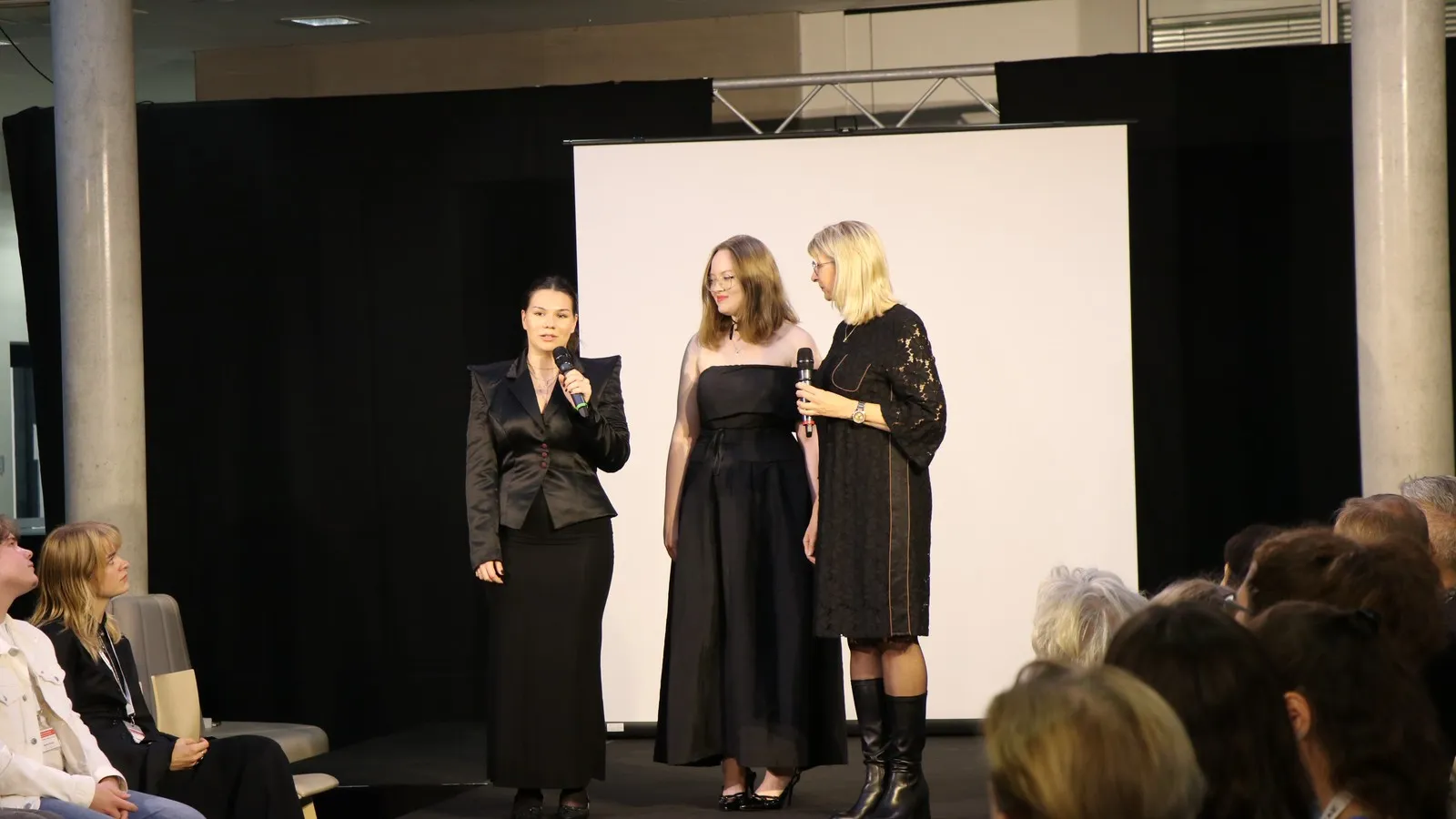Josie Schwänke und Noale Reichstein erklären auf der Bühne ihre Designs mit der Lehrerin Ursula Dreyer.