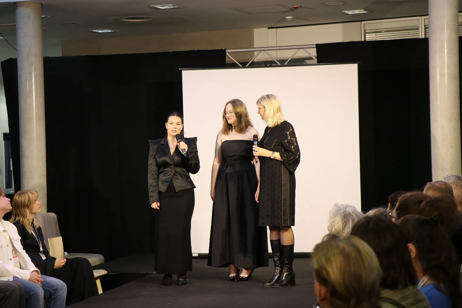 Josie Schwänke und Noale Reichstein erklären auf der Bühne ihre Designs mit der Lehrerin Ursula Dreyer.