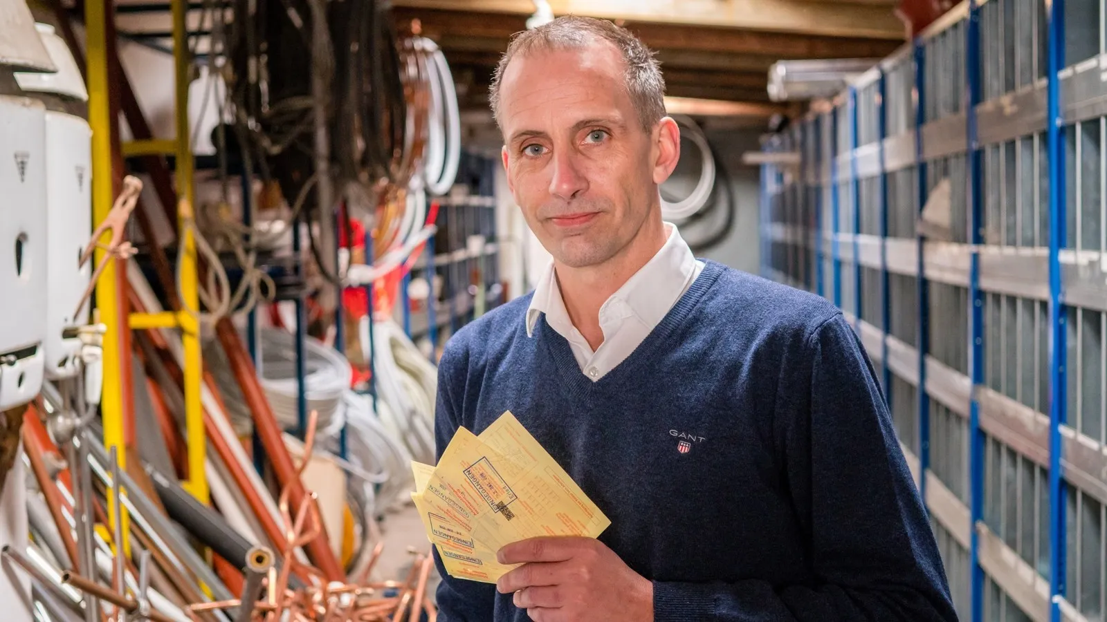 Foto von Kai Schaupmann mit gelben Scheinen in der Hand in einer Werkstatt.