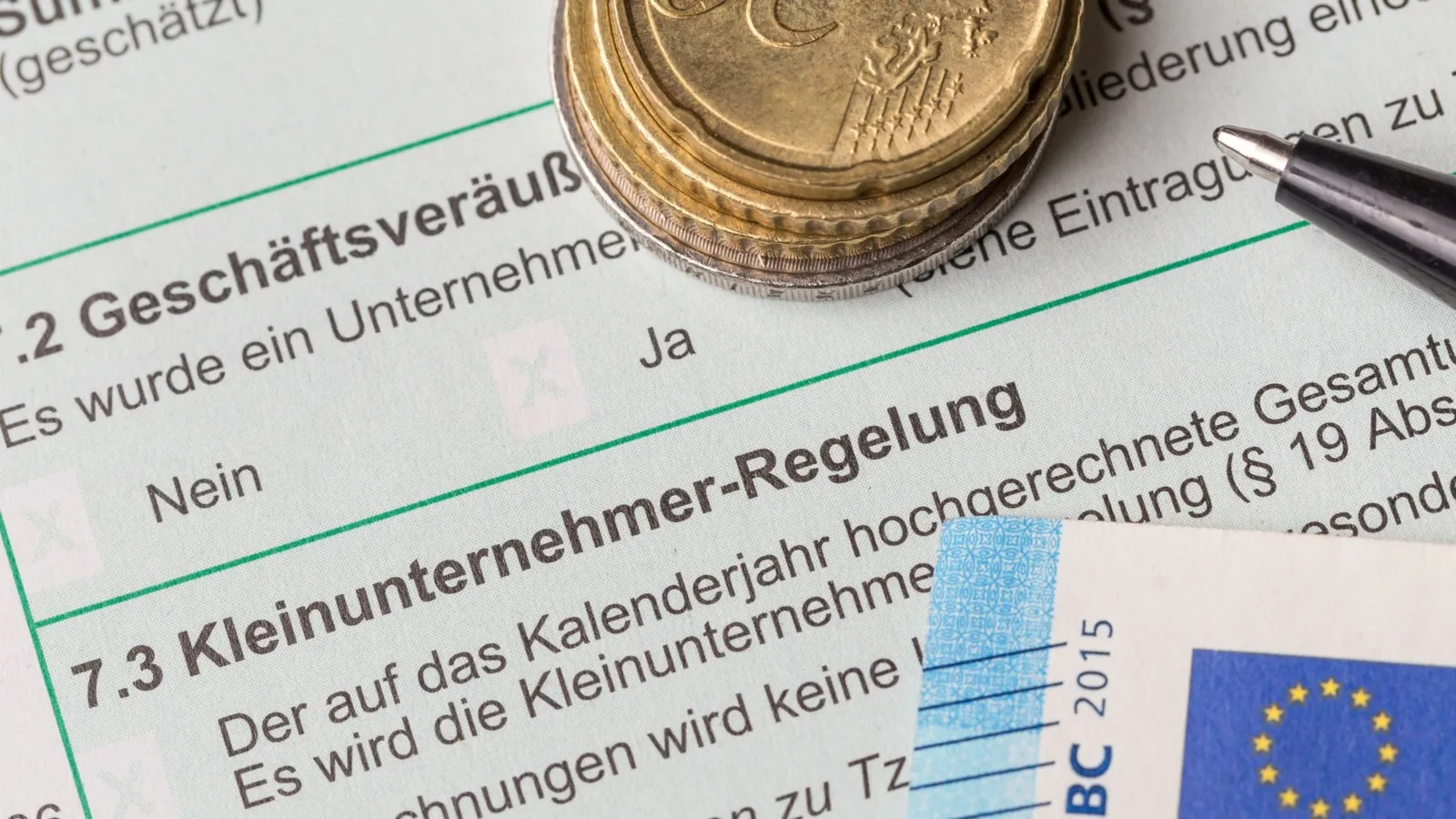 Ein Dokument zur Kleinunternehmer-Regelung, darauf liegen Münzen und ein 20 Euro Schein.
