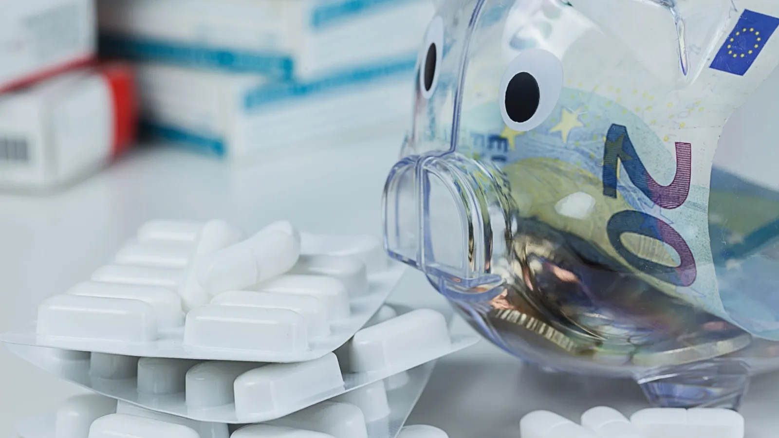 Ein 20 Euro-Schein steckt in einem durchsichtigen Sparschwein, daneben liegen mehrere Blister und lose Tabletten.