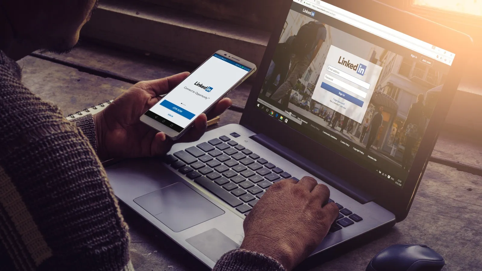Ein Mann sitzt an einem Laptop und hält gleichzeitig ein Smartphone in der Hand.