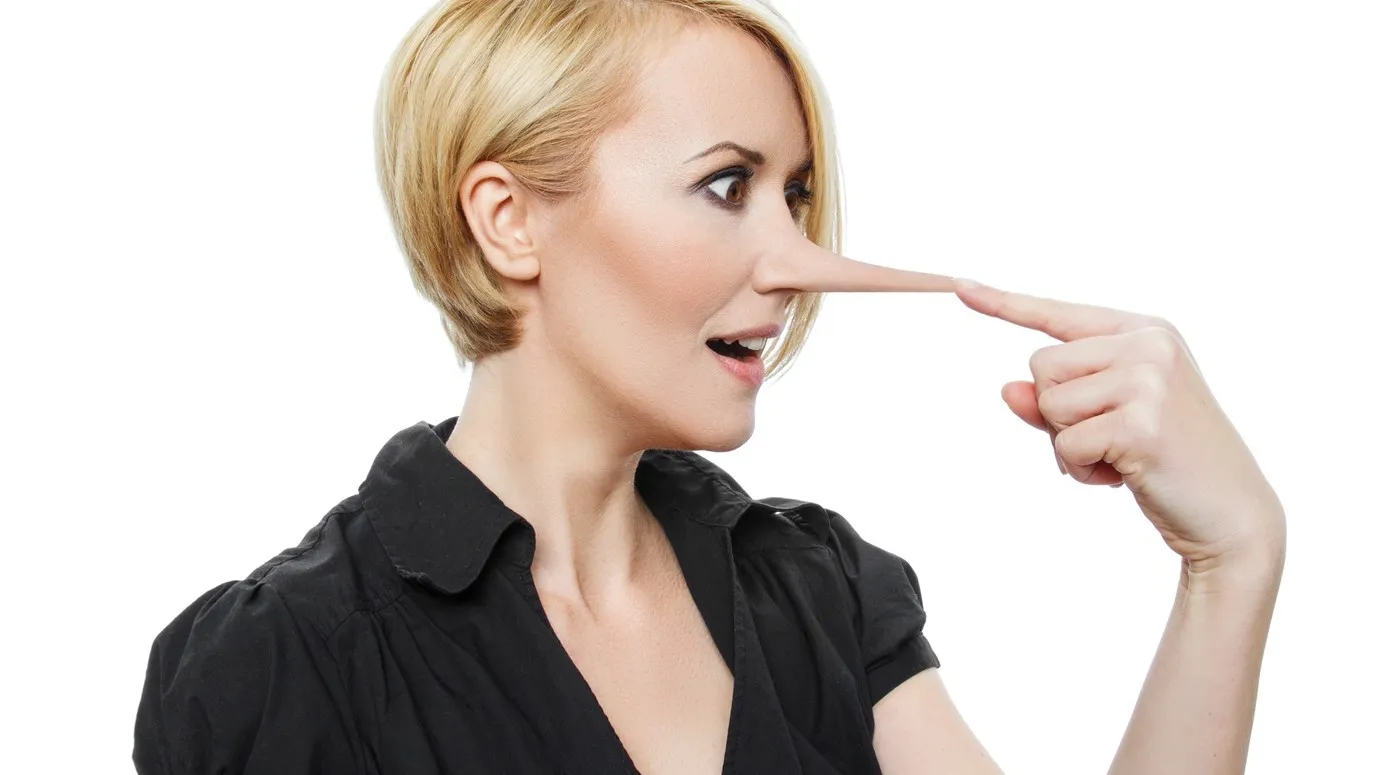 Eine blonde Frau ist von der Seite zu sehen. Sie hält sich ihren Zeigefinger an die Nase, welche lang gezogen ist.