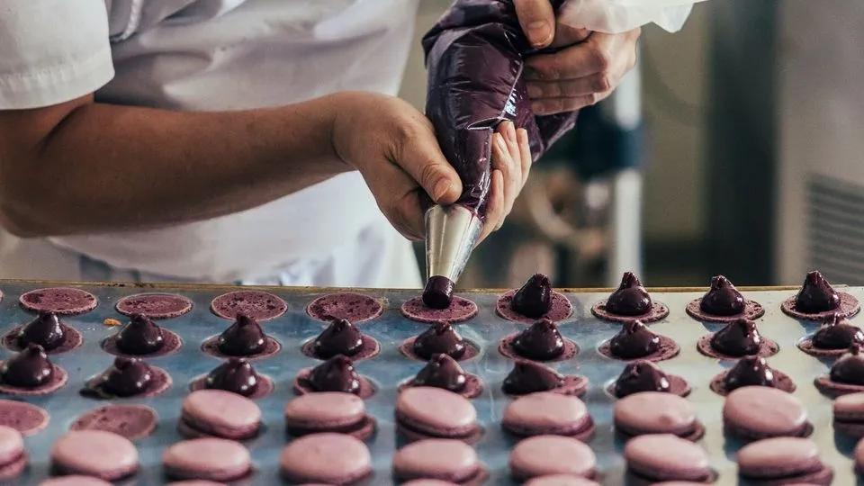 Fokussiert füllt Konditormeister (Maître Pâtissier) Serge Maranzana Macarons Cassis mit einer fruchtigen Ganache.