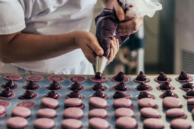 Fokussiert füllt Konditormeister (Maître Pâtissier) Serge Maranzana Macarons Cassis mit einer fruchtigen Ganache.