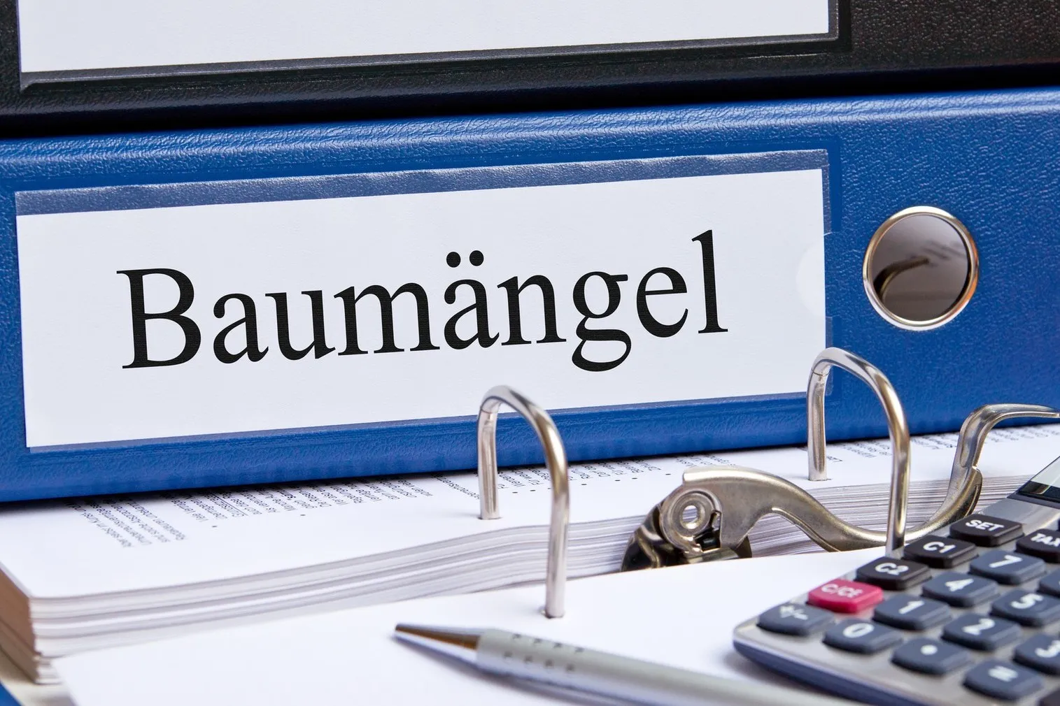 Ein blauer Ordner mit der Aufschrift "Baumängel" liegt auf einem Tisch.