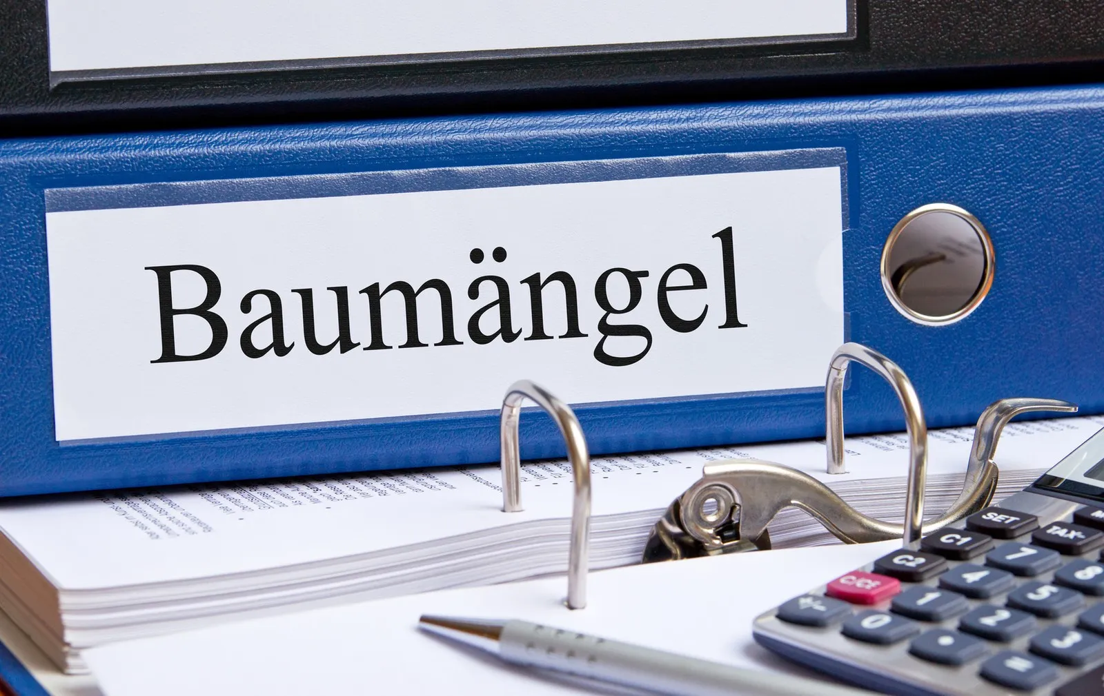 Ein blauer Ordner mit der Aufschrift "Baumängel" liegt auf einem Tisch.