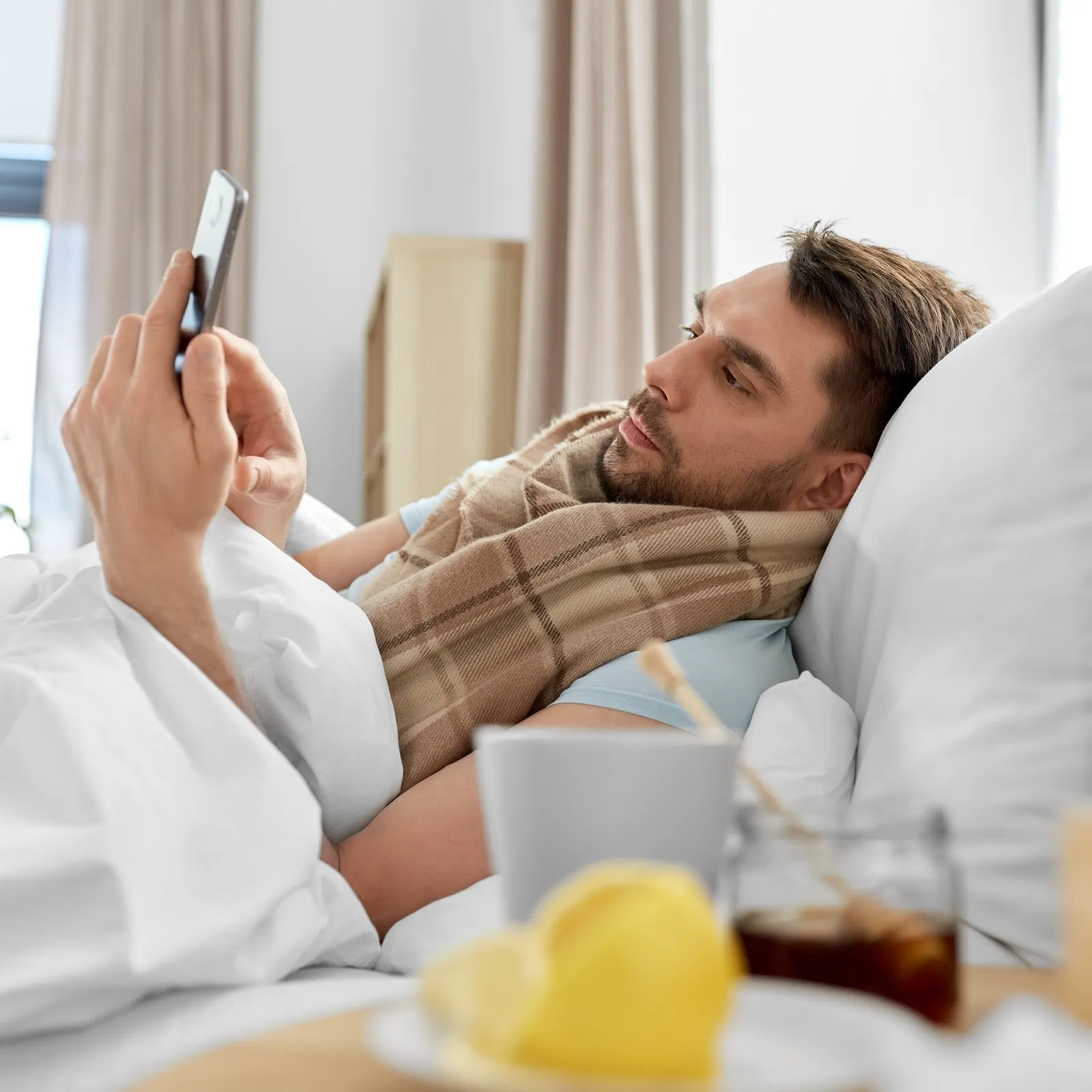 kranker Mann liegt im Bett und tippt auf sein Smartphone