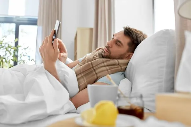 kranker Mann liegt im Bett und tippt auf sein Smartphone