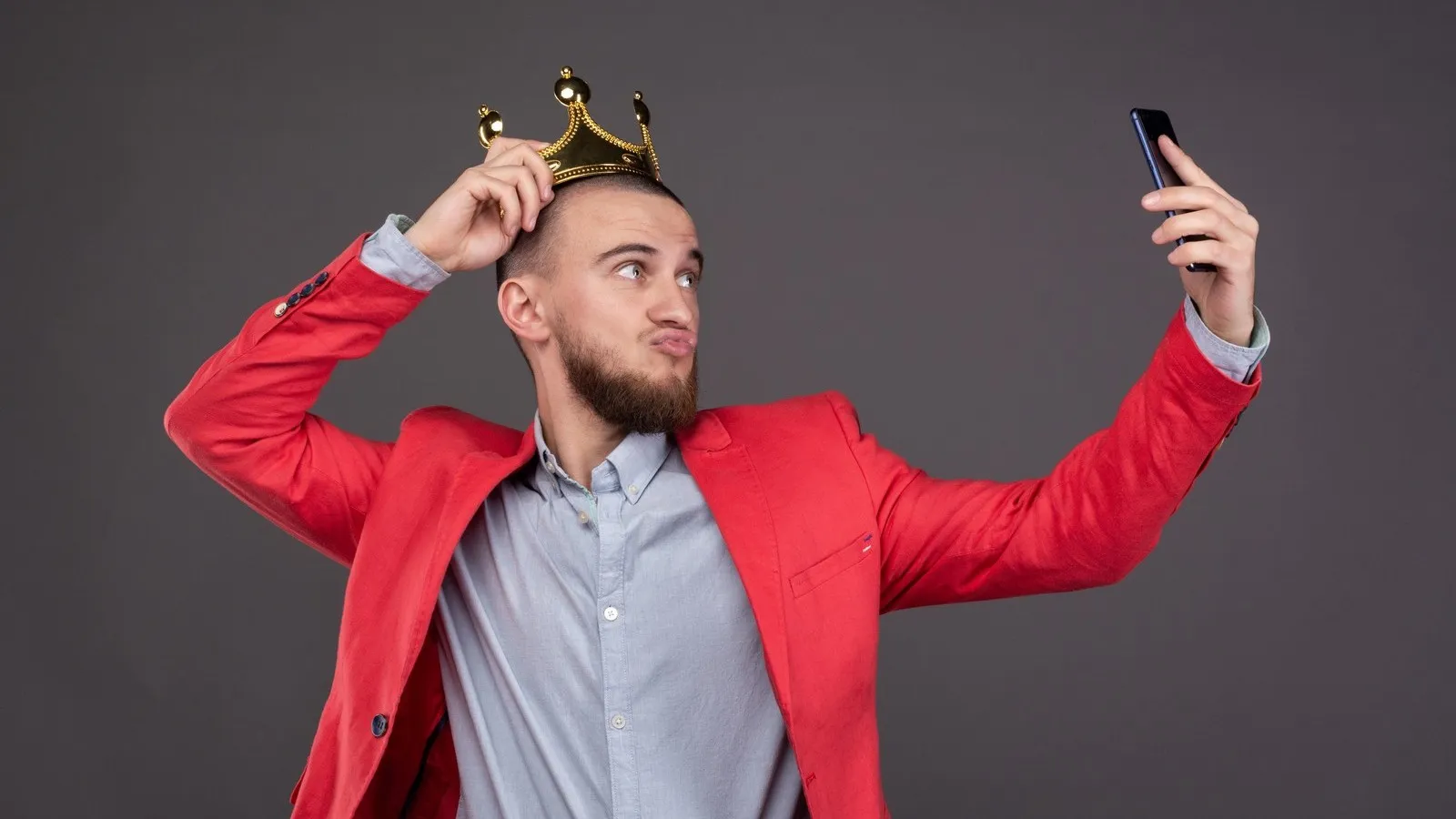 Mann mit goldener Krone auf dem Kopf macht ein Selfie.