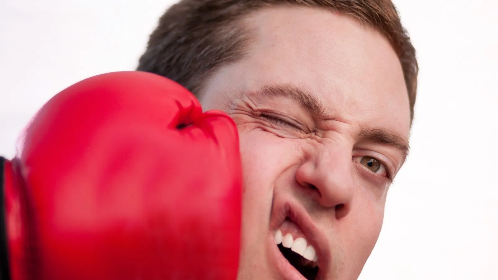 Ein Mann wird mit einem roten Boxhandschuh im Gesicht getroffen.