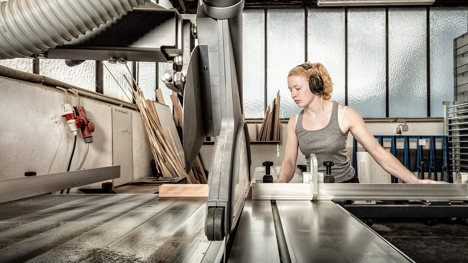 Tischlermeisterin Maxime Krämer schneidet in der Werkstatt mit einer großen Säge Holz zu.