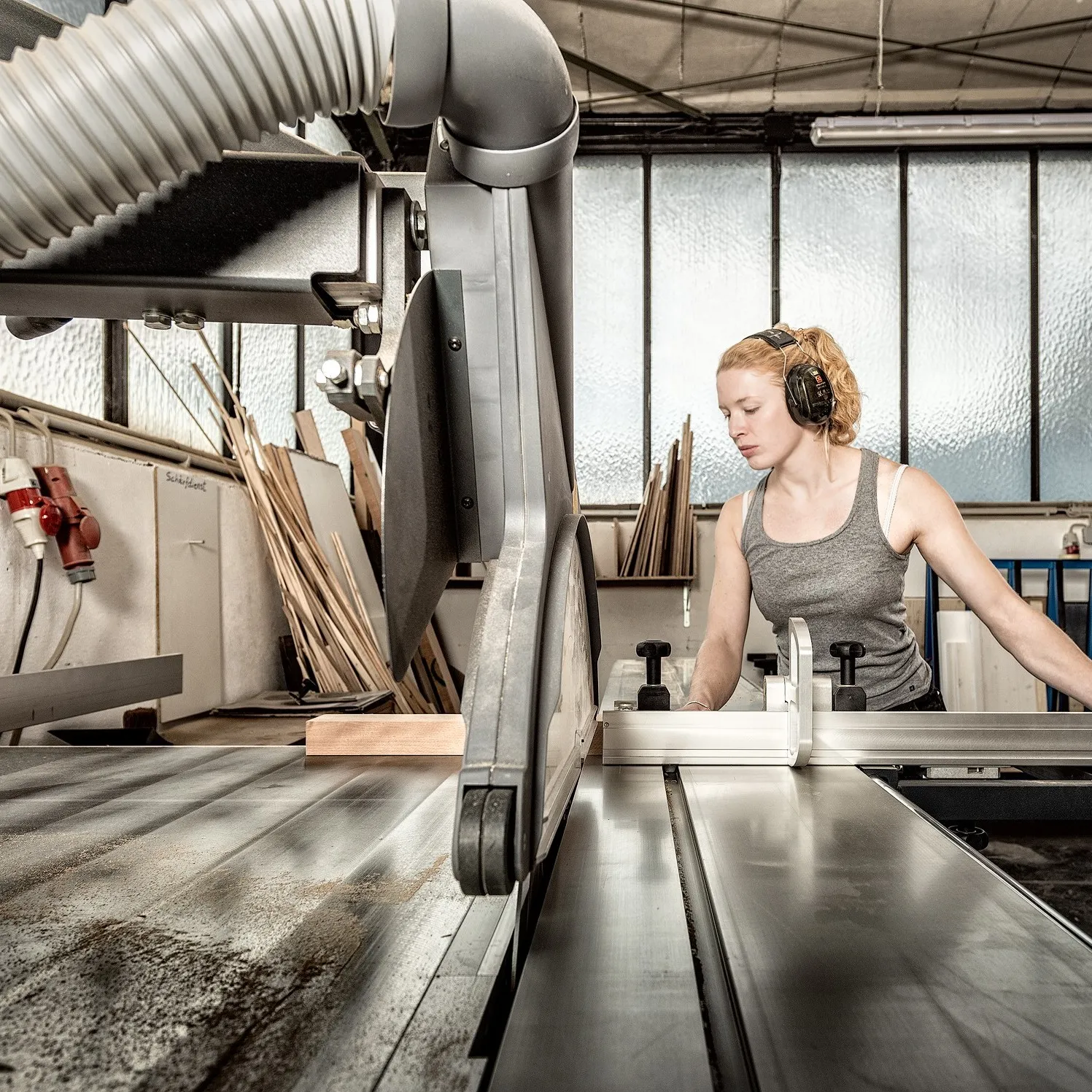 Tischlermeisterin Maxime Krämer schneidet in der Werkstatt mit einer großen Säge Holz zu.