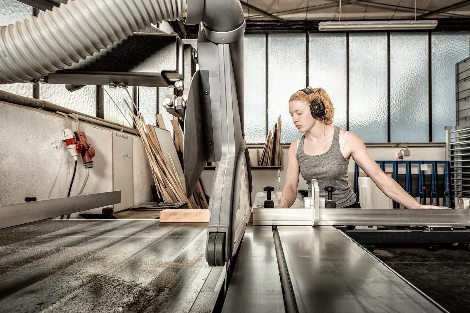 Tischlermeisterin Maxime Krämer schneidet in der Werkstatt mit einer großen Säge Holz zu.