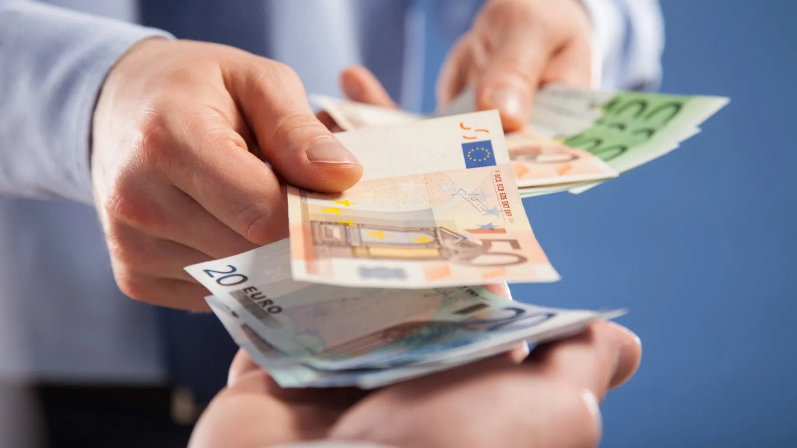 Jemand reicht einer anderen Personen einzelne Euro-Scheine.
