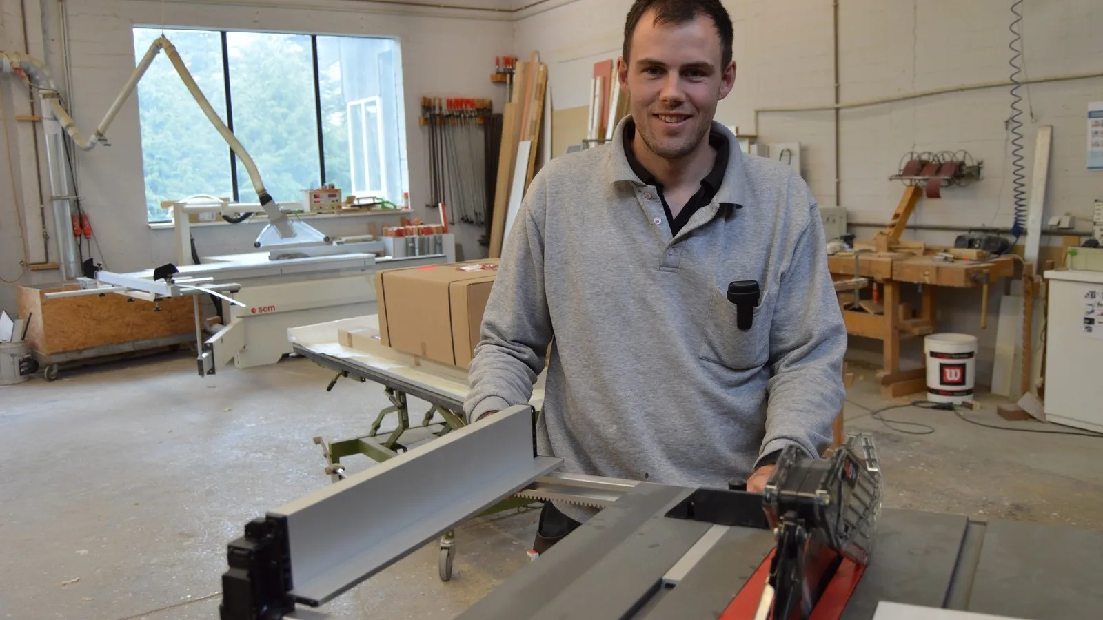 Ein Mann steht vor der Milwaukee Fuel M18 FTS210 Tischkreissäge in einer Werkstatthalle.