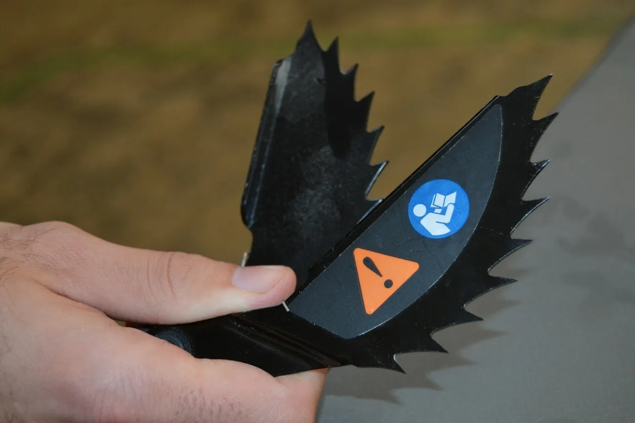 Eine Hand hält ein schwarzes zweigefächertes zackiges Metallteil in der Hand. Die "Holzfalle".