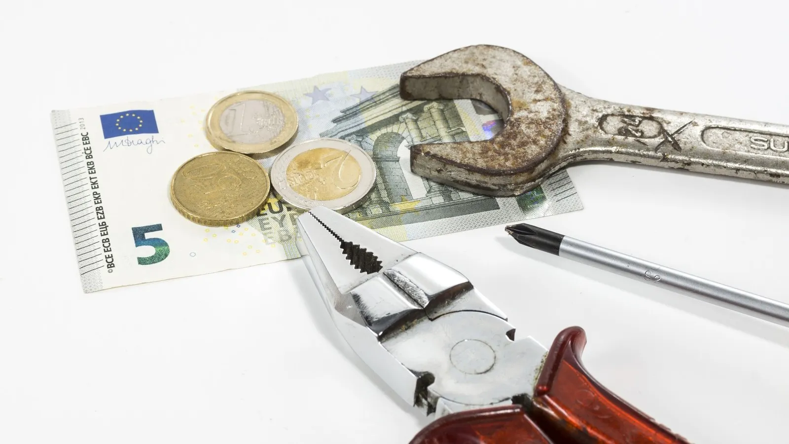 Ein 5 Euro Schein mit ein paar Münzen. Daneben liegen drei verschiedene Werkzeuge.