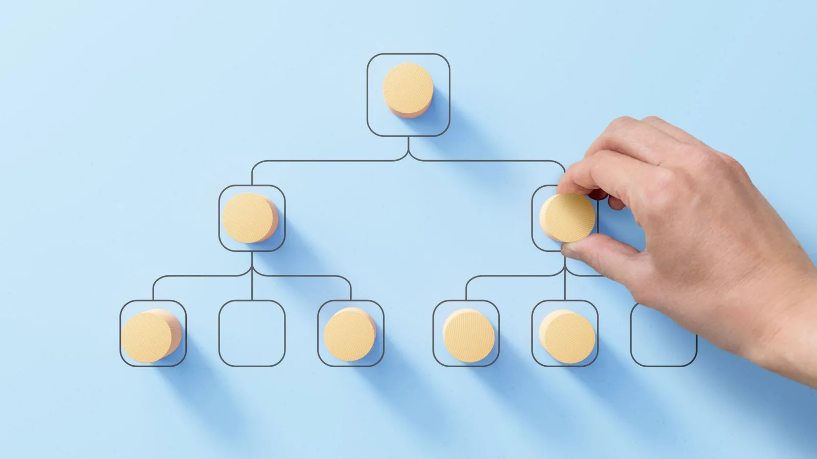 Kleine Holzstücke werden von einer Hand in einem Organigramm angeordnet. Der Hintergrund ist blau.