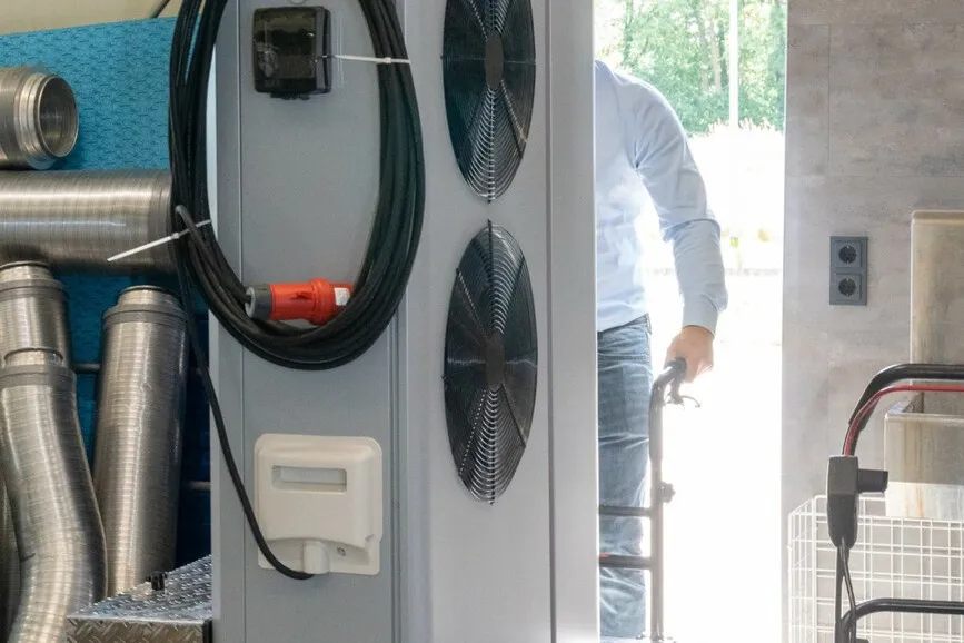 Die große graue Wärmepumpe steht auf einem klappbaren Transportwagen.