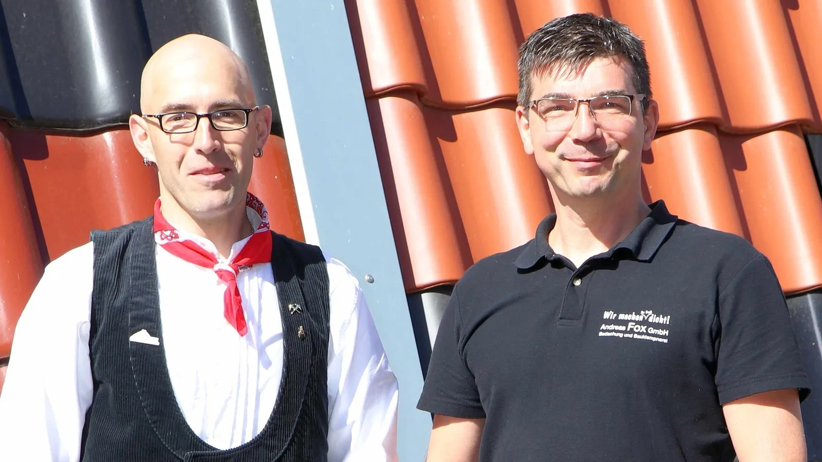 Foto von zwei Männern, die vor einem Dach nebeneinander stehen.