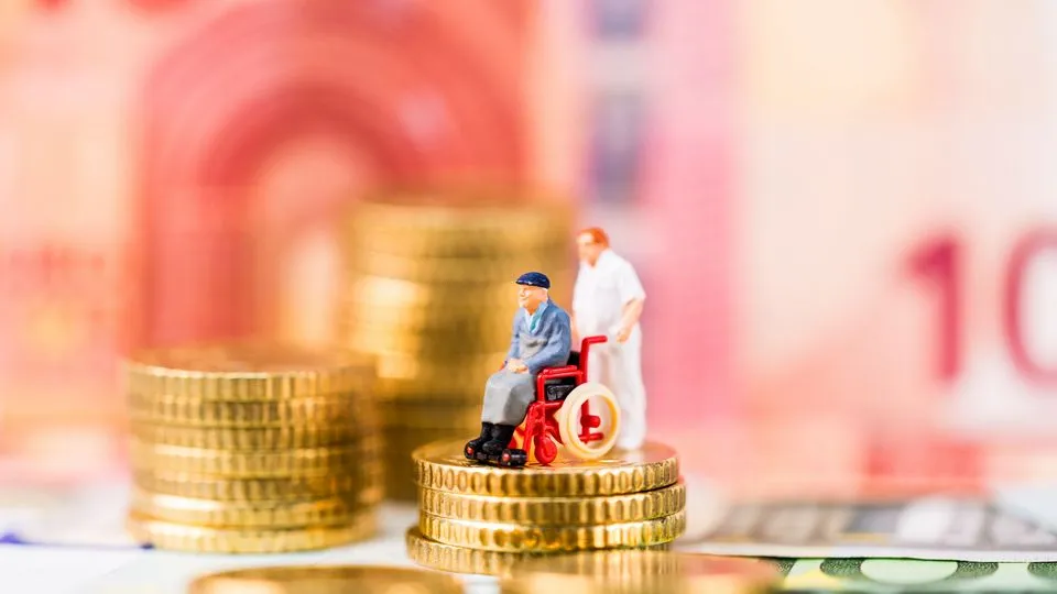 Ein Pflegebedürftiger im Rollstuhl und eine Pflegekraft stehen vor einer Kulisse aus Geld - darunter ein 10-Euro-Schein und diverse Euro-Münzen.
