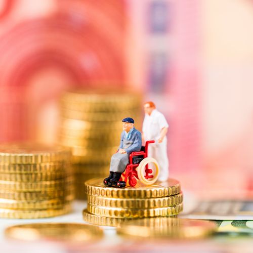Ein Pflegebedürftiger im Rollstuhl und eine Pflegekraft stehen vor einer Kulisse aus Geld - darunter ein 10-Euro-Schein und diverse Euro-Münzen.