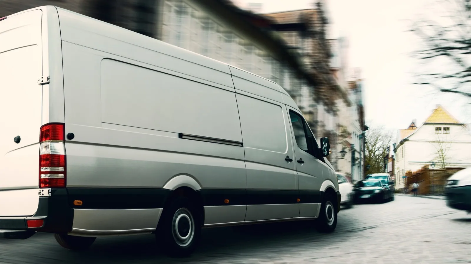 Ein grauer Transporter fährt eine Straße entlang. Der Hintergrund ist verwischt.