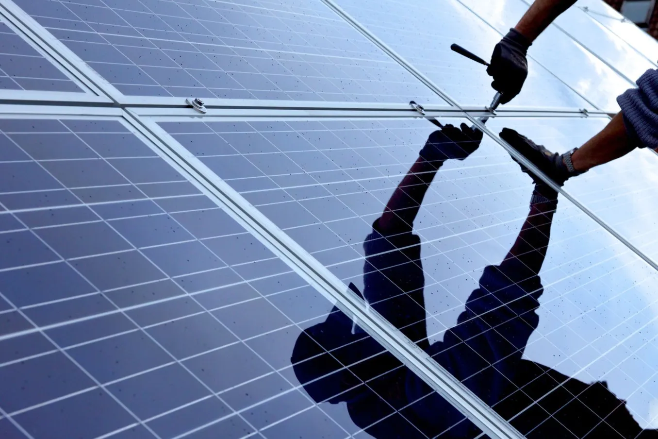 Nahaufnahme einer PV-Anlage mit dem Spiegelbild eines Handwerkers, die sie grad installiert.