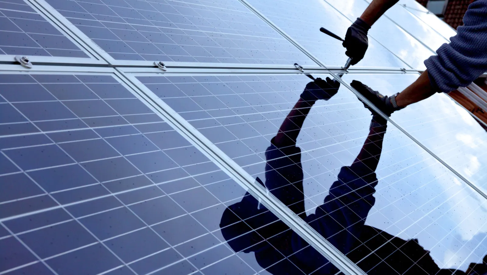 Nahaufnahme einer PV-Anlage mit dem Spiegelbild eines Handwerkers, die sie grad installiert.