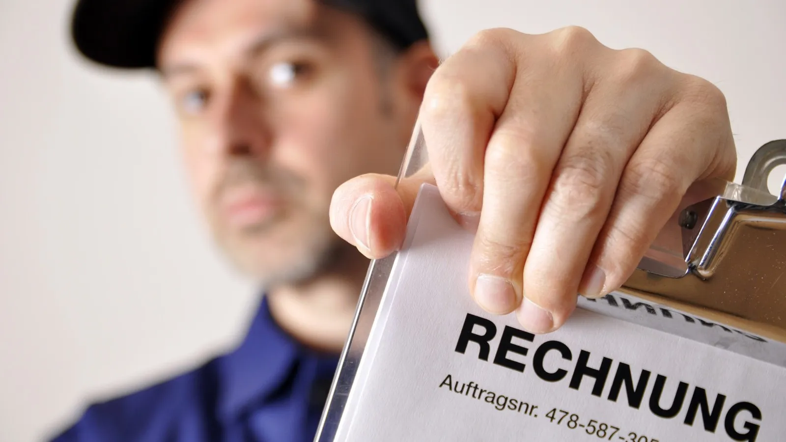Ein Mann mit einer Cap hält ein Dokument mit der Aufschrift "Aufschrift" in die Kamera.
