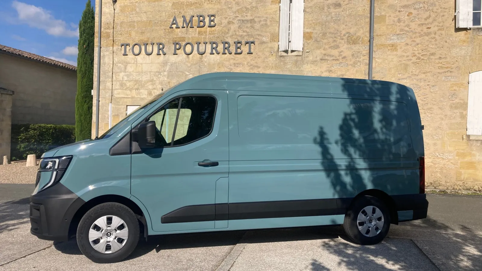 Seitenansicht: Der Master E-Tech Electric in grau-blau steht vor einem Gebäude mit der Aufschrift "AMBE TOUR POURRET".