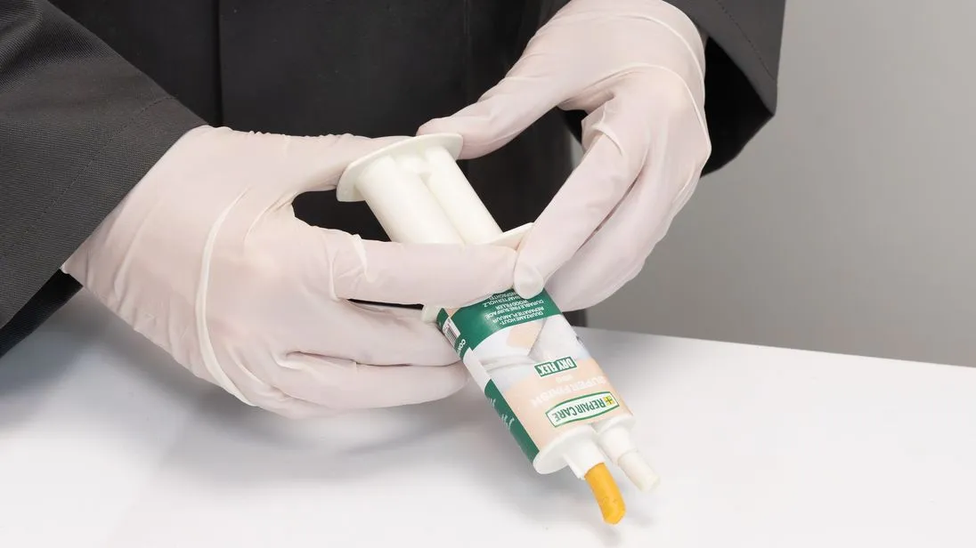 Hände in Handschuhen mit einen Spritzpistole aus der eine Paste herauskommt.