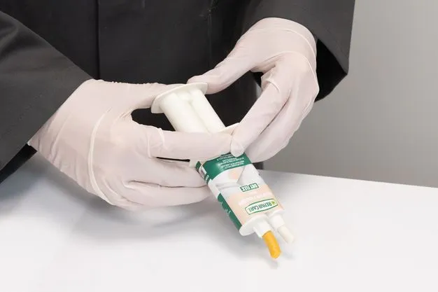 Hände in Handschuhen mit einen Spritzpistole aus der eine Paste herauskommt.