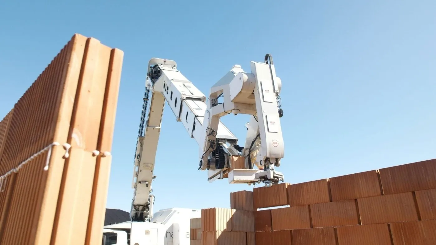 Ein weißer kranartiger Roboter verbaut optimierte Hintermauerziegel.