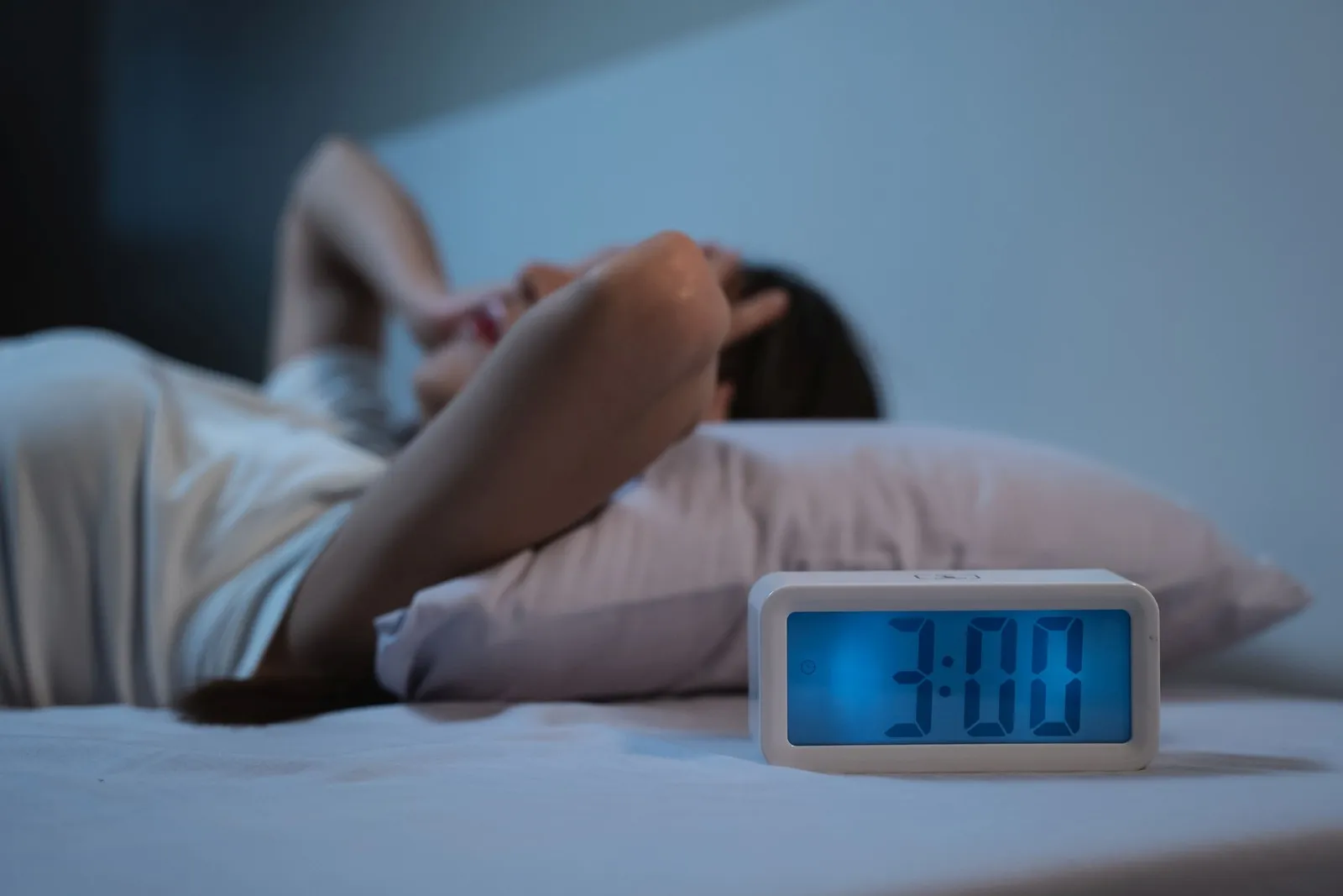 Eine Frau liegt nachts wach im Bett. Ein Wecker neben dem Bett zeigt an, dass es 3 Uhr ist.