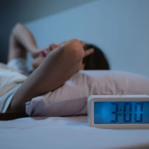 Eine Frau liegt nachts wach im Bett. Ein Wecker neben dem Bett zeigt an, dass es 3 Uhr ist.
