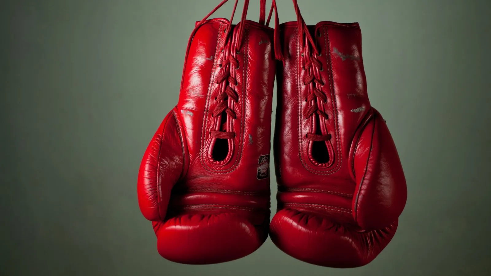 Rote Boxhandschuhe hängen vor einem grauen Hintergrund.