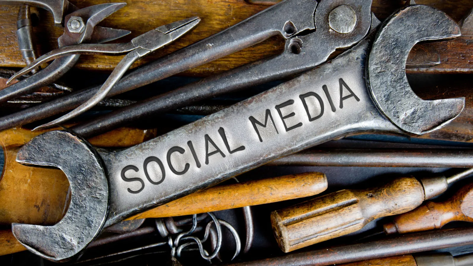 Eine Nahaufnahme von mehreren Werkzeugen. In der Mitte liegt ein Schraubenschlüssel mit der Aufschrift "Social Media" Drumherum sind mehrere Zangen und Schraubenzieher.