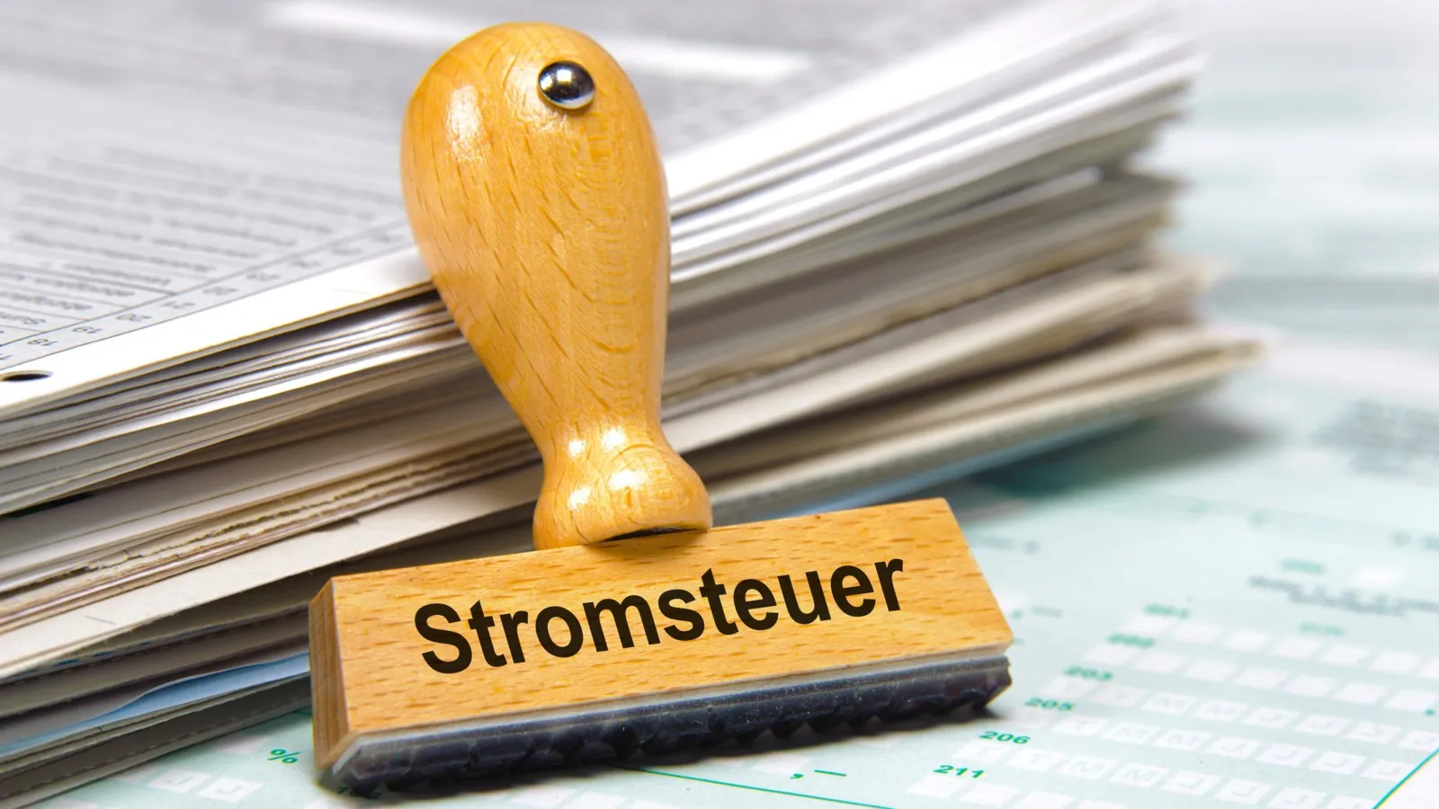 Ein Holzstempel mit der Aufschrift "Stromsteuer" angelehnt an einen Haufen Blätter.