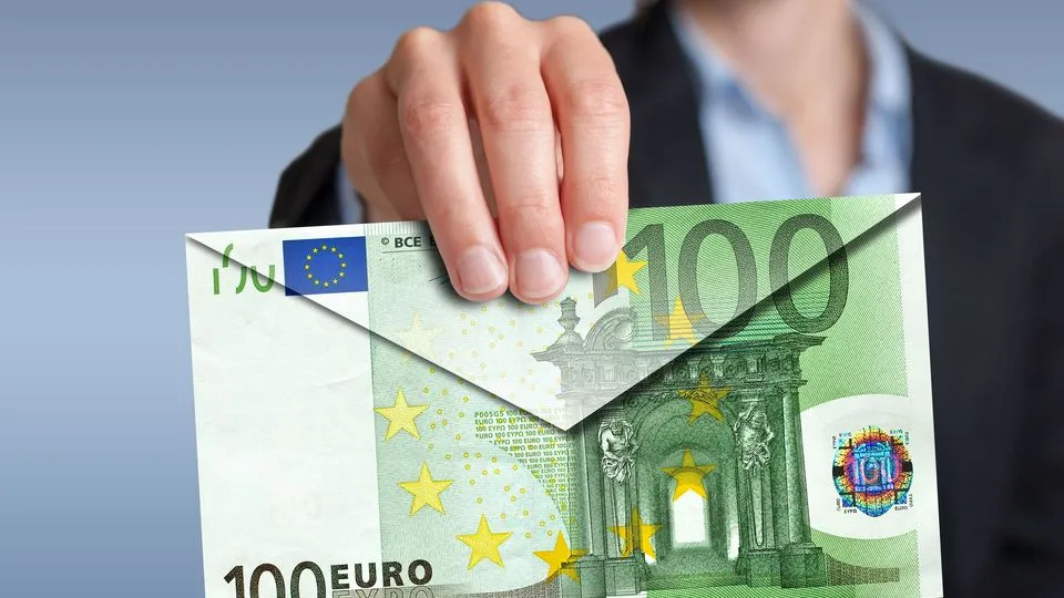 Eine Frau hält einen Briefumschlag in Richtung einer Kamera. Der Briefumschlag wurde aus einem großen 100-Euro-Schein gefaltet.