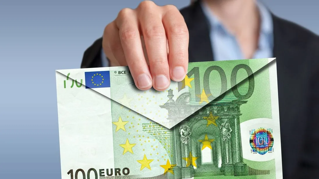 Eine Frau hält einen Briefumschlag in Richtung einer Kamera. Der Briefumschlag wurde aus einem großen 100-Euro-Schein gefaltet.