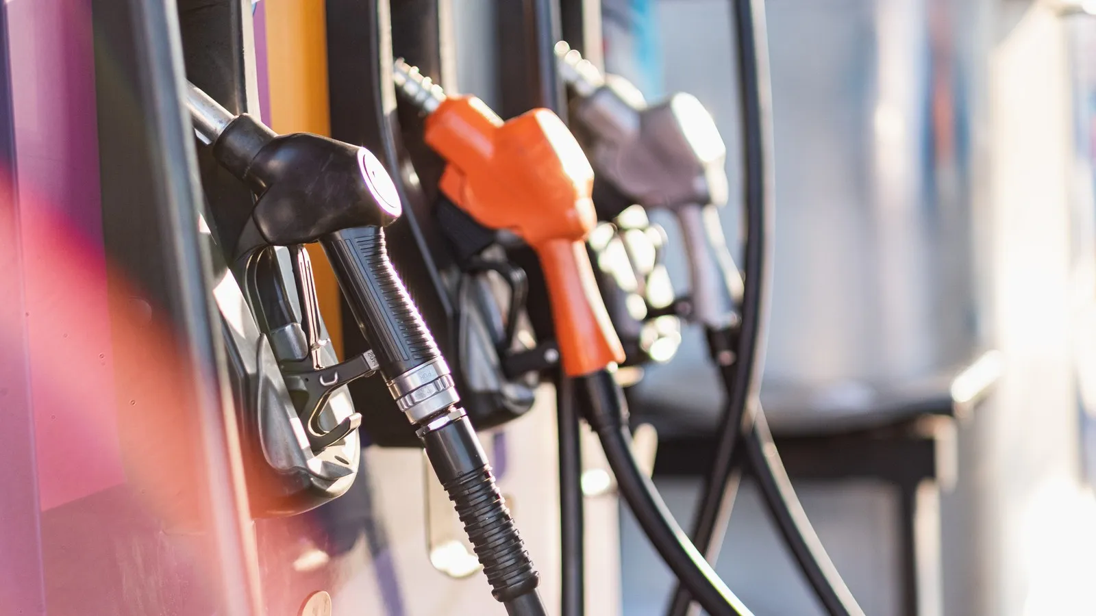 Drei verschieden farbige Zapfhähne hängen an einer Zapfsäule einer Tankstelle.