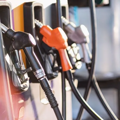 Drei verschieden farbige Zapfhähne hängen an einer Zapfsäule einer Tankstelle.