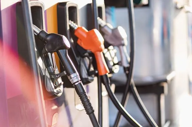Drei verschieden farbige Zapfhähne hängen an einer Zapfsäule einer Tankstelle.