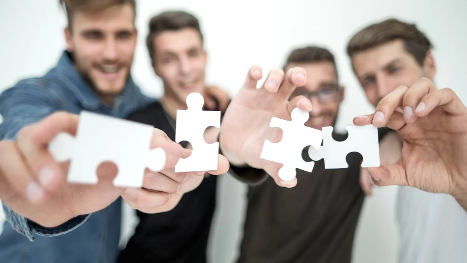 Eine Gruppe junger Männer halten jeweils ein weißes Puzzleteil ins Bild.